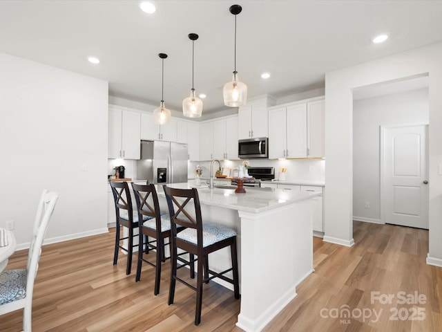 5532 Muckross Ln, Fort Mill, SC 29707 - kitchen with an island with sink, light wood-style flooring, white cabinetry, a breakfast bar, and appliances with stainless steel finishes