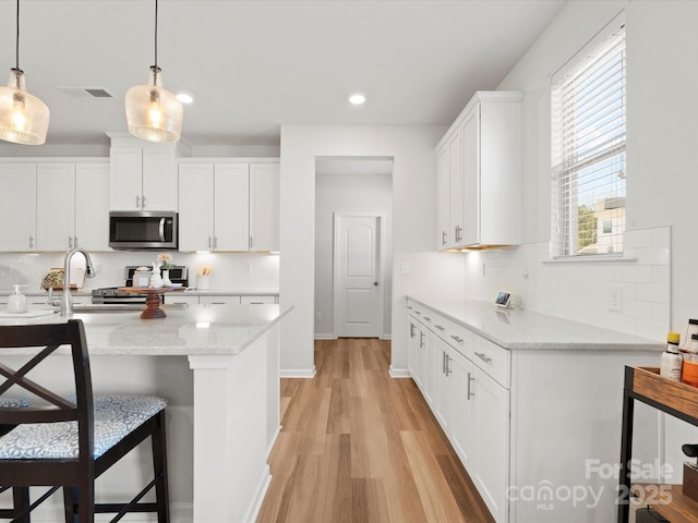 5532 Muckross Ln, Fort Mill, SC 29707 - kitchen with visible vents, white cabinets, a sink, light wood finished floors, and stainless steel appliances