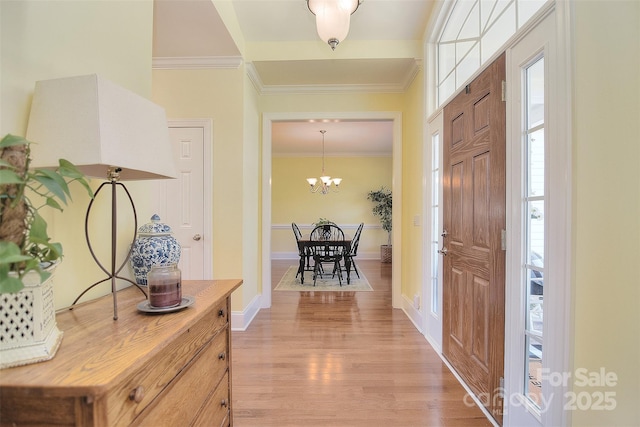 foyer entrance featuring crown molding, light wood-style flooring, a notable chandelier, and baseboards