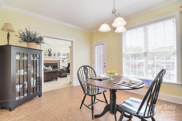 dining room with baseboards, ornamental molding, a chandelier, light tile patterned floors, and a tile fireplace