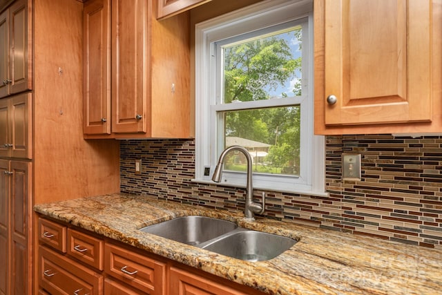 kitchen with light stone counters, a sink, brown cabinets, and tasteful backsplash