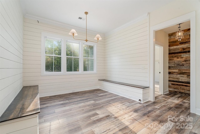 unfurnished dining area featuring an inviting chandelier, wood walls, wood finished floors, and visible vents
