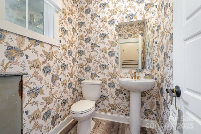 bathroom with wallpapered walls, toilet, wood finished floors, and baseboards