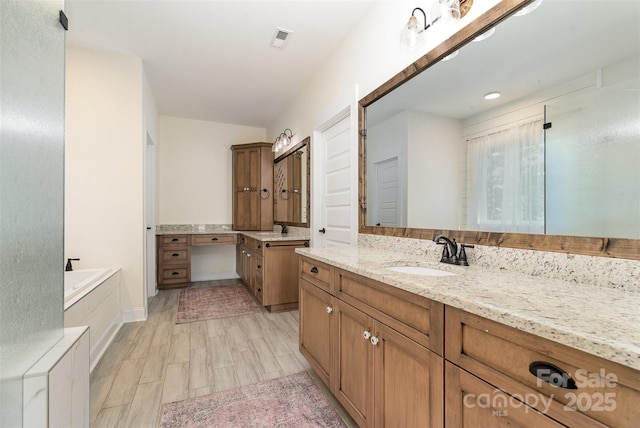 bathroom featuring a bath, visible vents, wood finished floors, and a sink