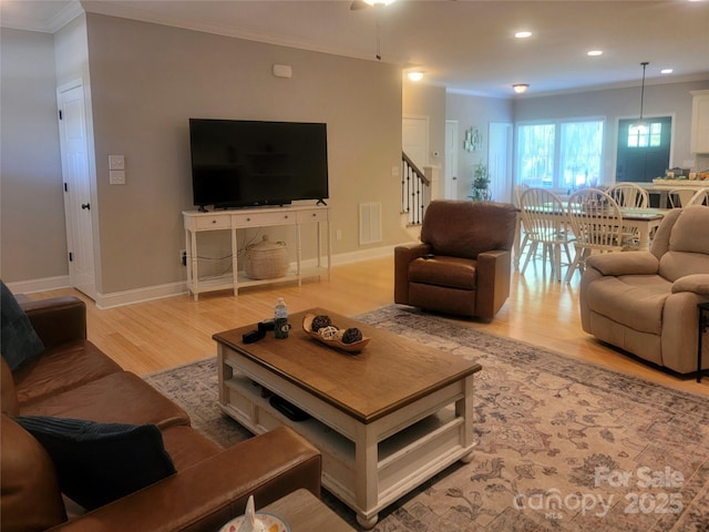 living area featuring crown molding, baseboards, light wood-style floors, and stairs