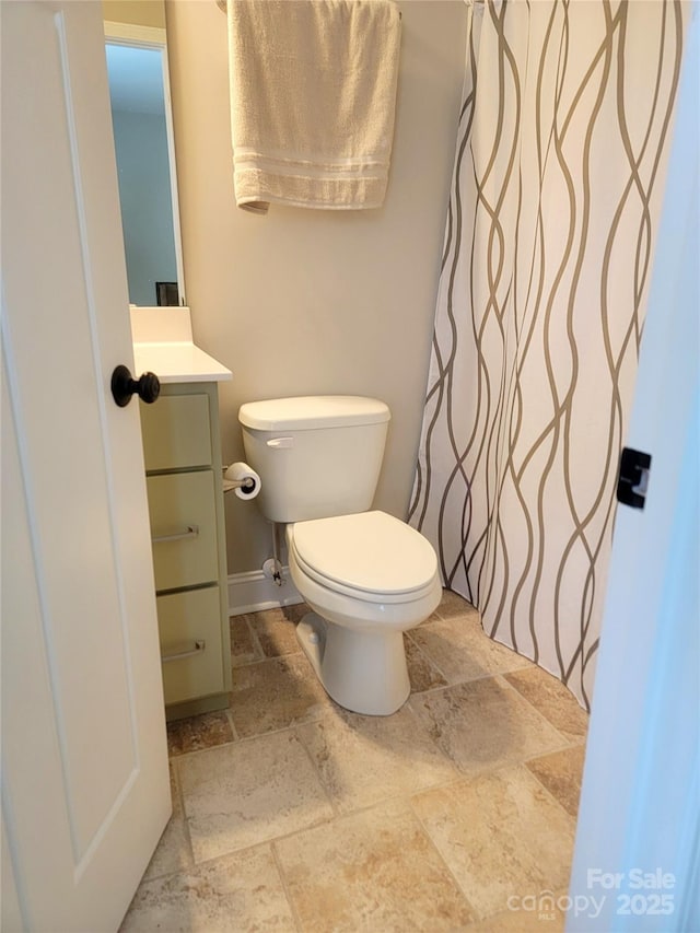 full bath featuring stone tile floors, vanity, a shower with curtain, toilet, and baseboards