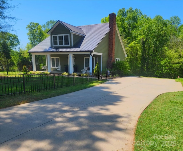 view of front facade with covered porch, metal roof, a front yard, a chimney, and concrete driveway