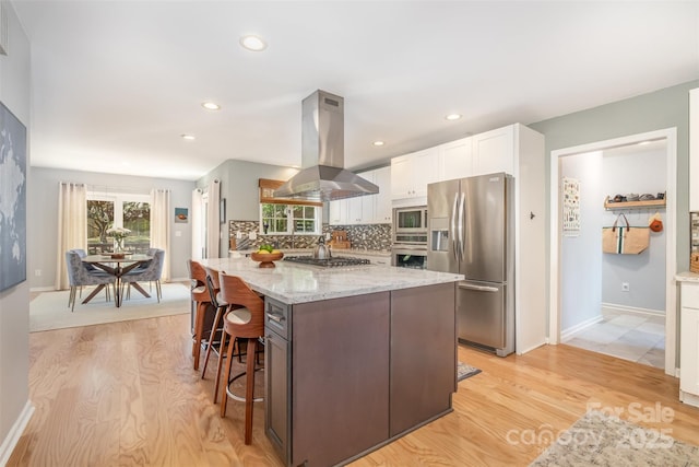 127 Fantasy Ln, Mooresville, NC 28117 - kitchen with stainless steel appliances, island range hood, light wood-style floors, white cabinets, and recessed lighting