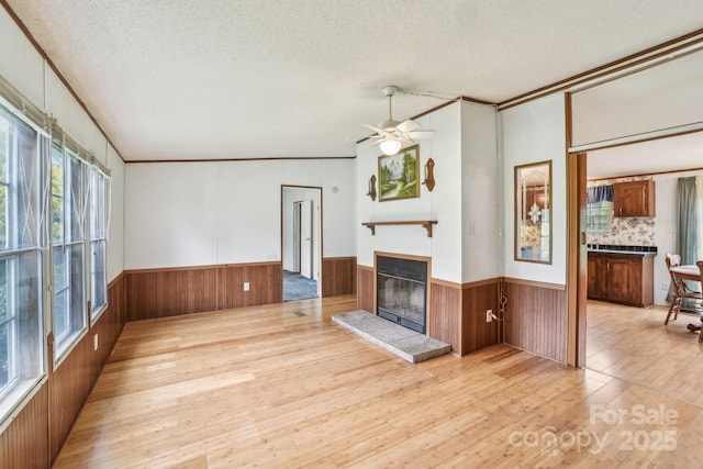 unfurnished living room with a wainscoted wall, hardwood / wood-style floors, a glass covered fireplace, and a textured ceiling