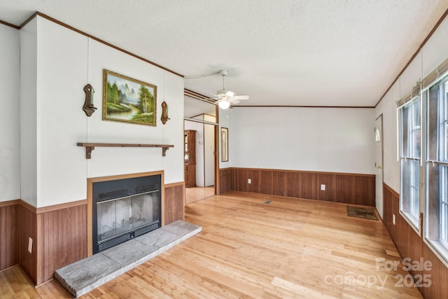 unfurnished living room with a textured ceiling, ornamental molding, a glass covered fireplace, wood finished floors, and wainscoting