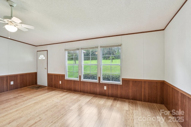 empty room with a textured ceiling, wood walls, wainscoting, hardwood / wood-style floors, and ceiling fan