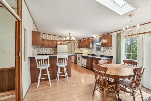 dining space featuring a notable chandelier, wallpapered walls, vaulted ceiling with skylight, a textured ceiling, and light wood-style floors