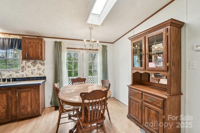 dining area with crown molding, vaulted ceiling with skylight, a notable chandelier, and light wood-style floors