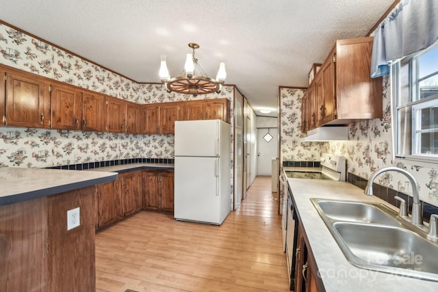 kitchen featuring a notable chandelier, a sink, white appliances, a textured ceiling, and wallpapered walls