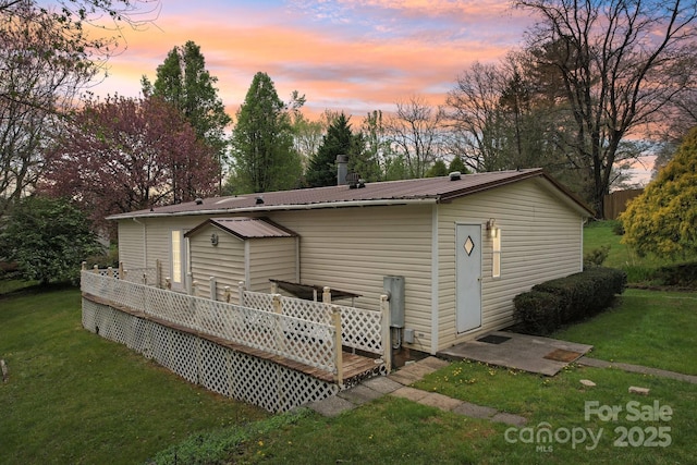 back of property with a wooden deck, metal roof, and a lawn
