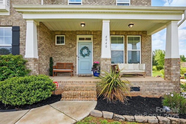 entrance to property featuring a porch and brick siding