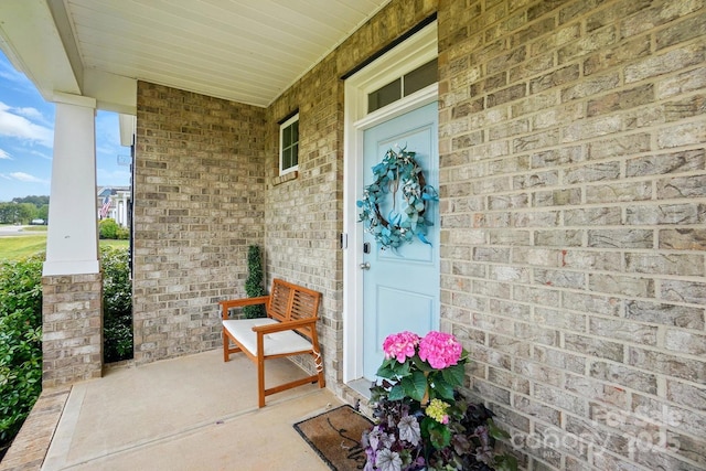 view of exterior entry featuring a porch and brick siding