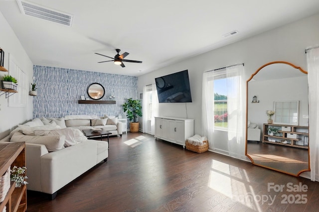living area featuring wallpapered walls, an accent wall, ceiling fan, visible vents, and dark wood-type flooring