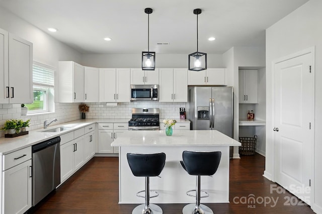 kitchen with a breakfast bar area, appliances with stainless steel finishes, a kitchen island, a sink, and dark wood-type flooring