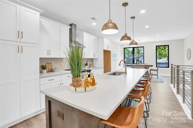 3449 Byrnes St, Charlotte, NC 28205 - kitchen featuring wall chimney exhaust hood, a sink, light wood-type flooring, a spacious island, and recessed lighting