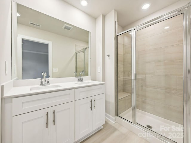 bathroom featuring a shower stall, double vanity, and recessed lighting
