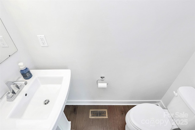 half bathroom with wood finished floors, visible vents, a sink, and toilet