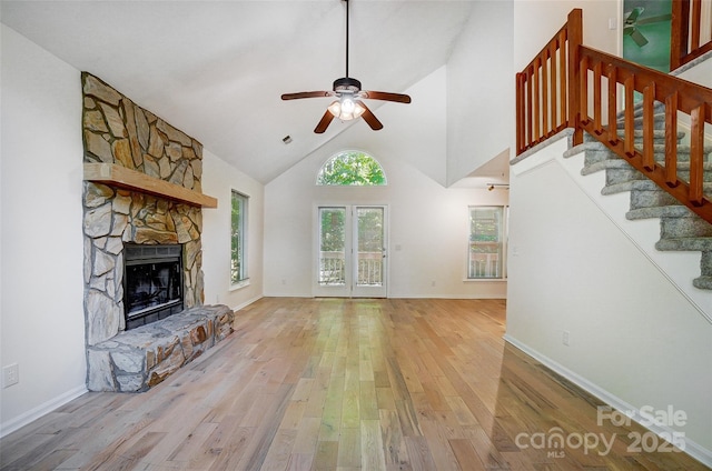 unfurnished living room featuring a ceiling fan, light wood-style floors, a fireplace, stairway, and high vaulted ceiling