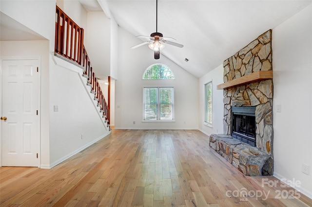 unfurnished living room featuring a fireplace, stairs, light wood-style floors, ceiling fan, and high vaulted ceiling