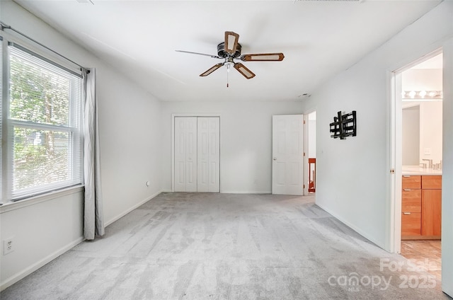 unfurnished bedroom featuring a closet, baseboards, ensuite bathroom, visible vents, and light colored carpet