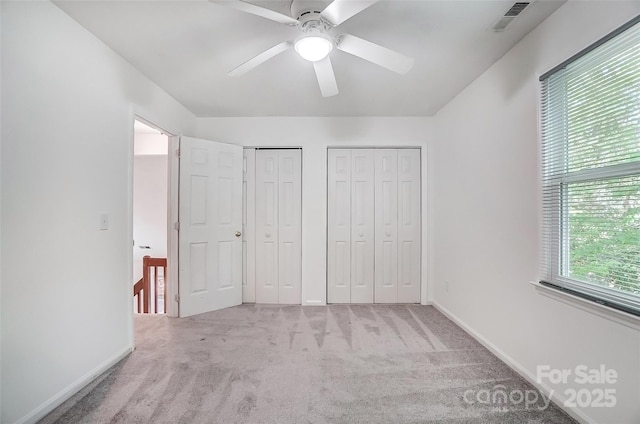 unfurnished bedroom featuring two closets, a ceiling fan, visible vents, carpet flooring, and baseboards