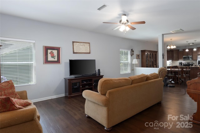living area featuring baseboards, visible vents, dark wood-style floors, and ceiling fan with notable chandelier