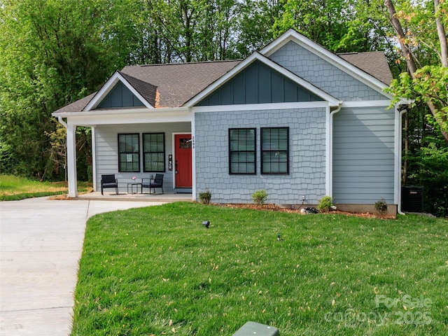 view of front of home with roof with shingles, covered porch, cooling unit, and a front yard