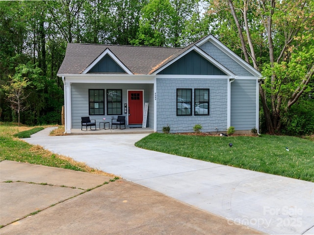 view of front facade with covered porch, concrete driveway, a shingled roof, and a front yard