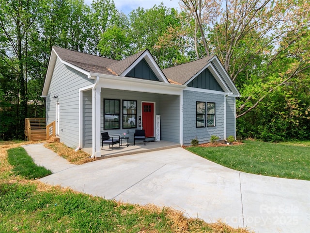 view of front of home with a porch, board and batten siding, roof with shingles, and a front yard