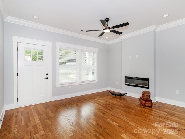 unfurnished living room with ornamental molding, a glass covered fireplace, wood finished floors, baseboards, and ceiling fan