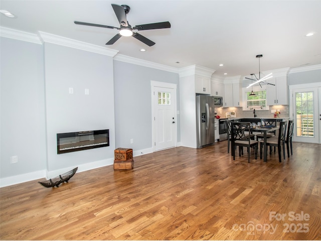 living area with crown molding, a ceiling fan, a glass covered fireplace, and light wood finished floors