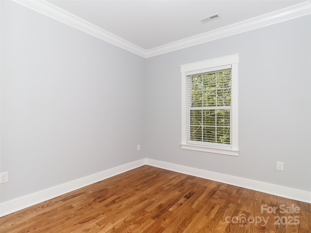 empty room with crown molding, baseboards, visible vents, and wood finished floors