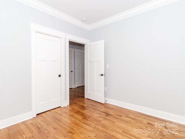 unfurnished bedroom featuring crown molding, light wood-style floors, baseboards, visible vents, and a closet