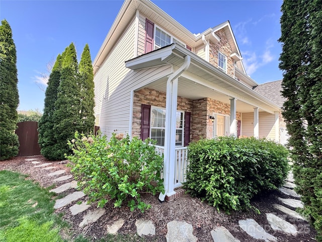 view of property exterior featuring stone siding, fence, and covered porch