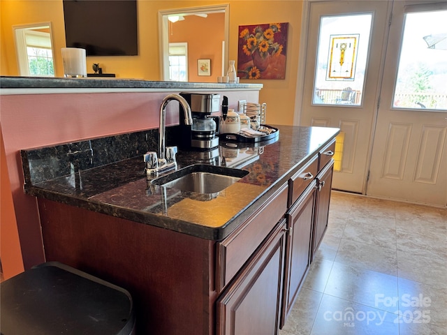 kitchen featuring light tile patterned flooring, dark brown cabinets, dark stone countertops, and a sink