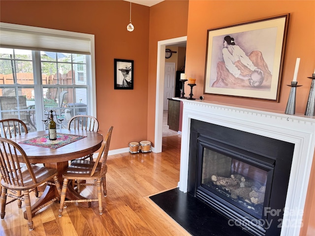 dining area featuring a fireplace with flush hearth, light wood-style floors, and baseboards