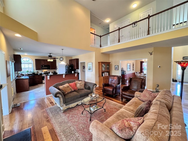 living room featuring light wood-style flooring, a high ceiling, and ceiling fan
