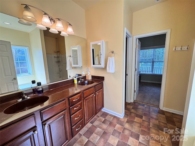 bathroom featuring baseboards, walk in shower, a sink, and double vanity