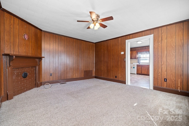 unfurnished living room with a ceiling fan, wooden walls, carpet, and baseboards