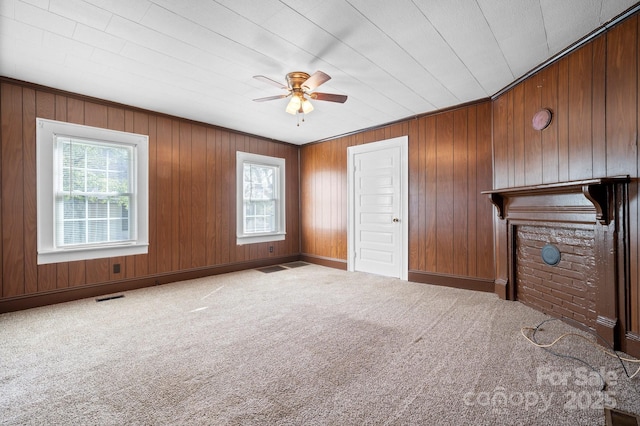unfurnished living room featuring a ceiling fan, wooden walls, visible vents, and carpet