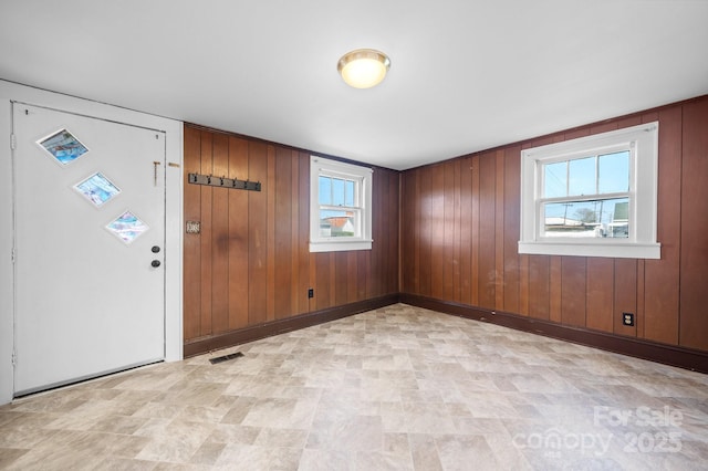 foyer with baseboards, wood walls, visible vents, and plenty of natural light