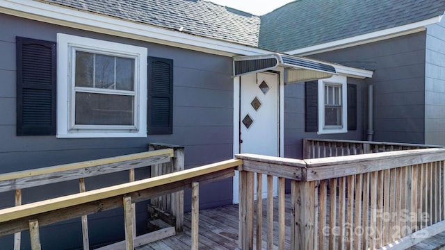 doorway to property with a wooden deck and roof with shingles