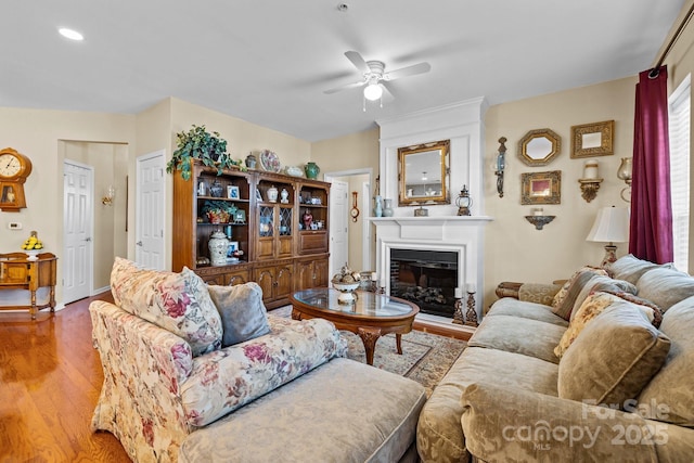 living room featuring a ceiling fan, a glass covered fireplace, and wood finished floors