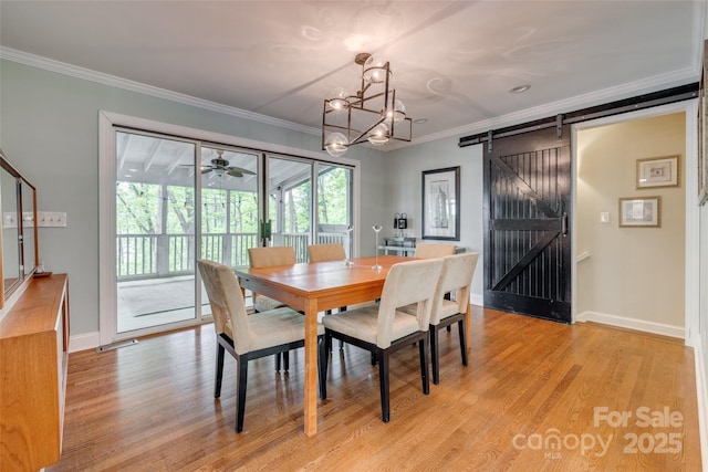 dining space featuring crown molding, light wood-type flooring, a barn door, a chandelier, and baseboards