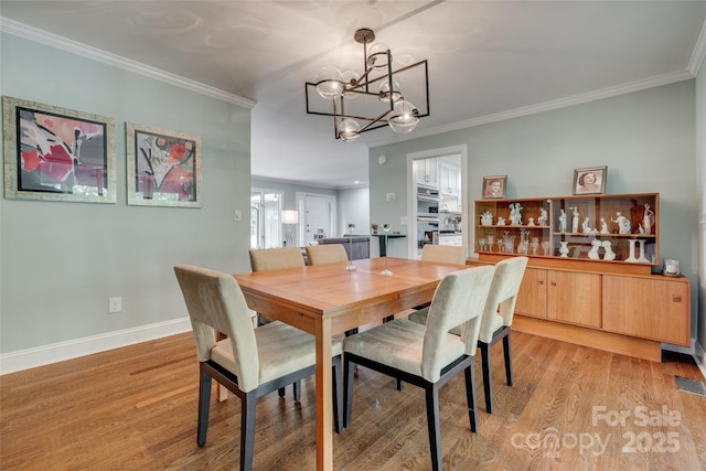 dining room with light wood-style floors, an inviting chandelier, crown molding, and baseboards